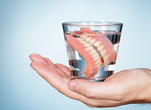 hand holding dentures in a glass of water